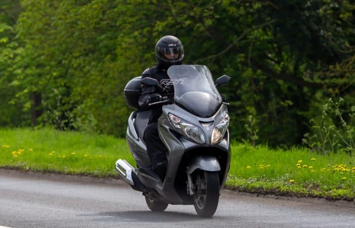 homme qui conduit un maxi scooter dans la foret 